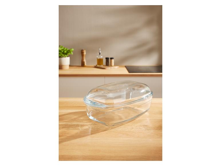 Sklenená zapekacia misa s vekom na kuchynskej linke s korením a rastlinou v pozadí.