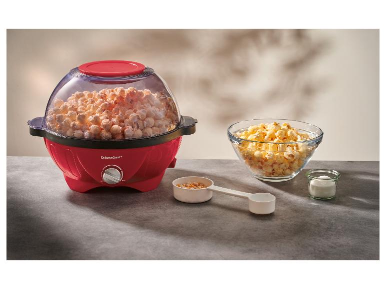 Červený popcornovač plný popcornu s miskou popcornu a prísadami na stole.