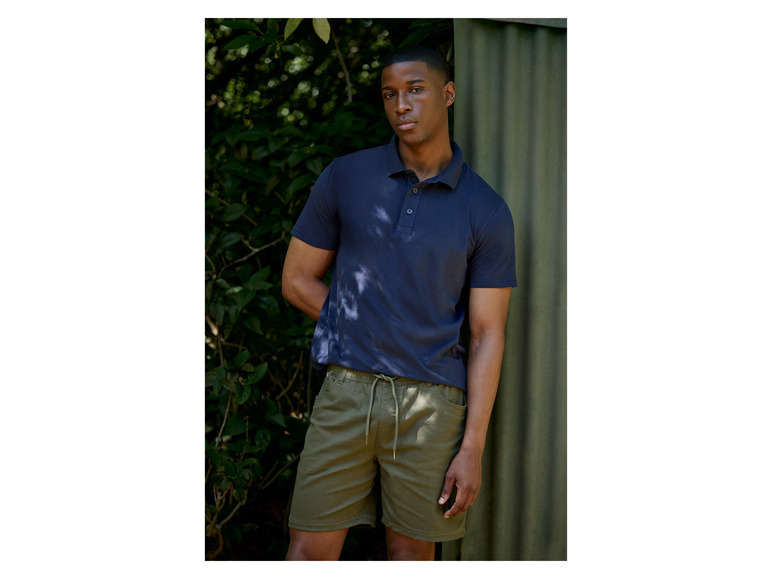 Muž v modrom poló a zelených šortkách.