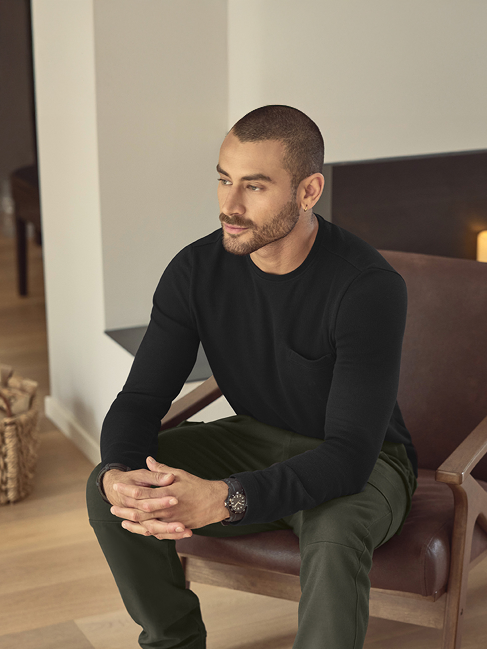 Muž v čiernom tričku s dlhým rukávom a zelených nohaviciach, sediaci na koženej stoličke