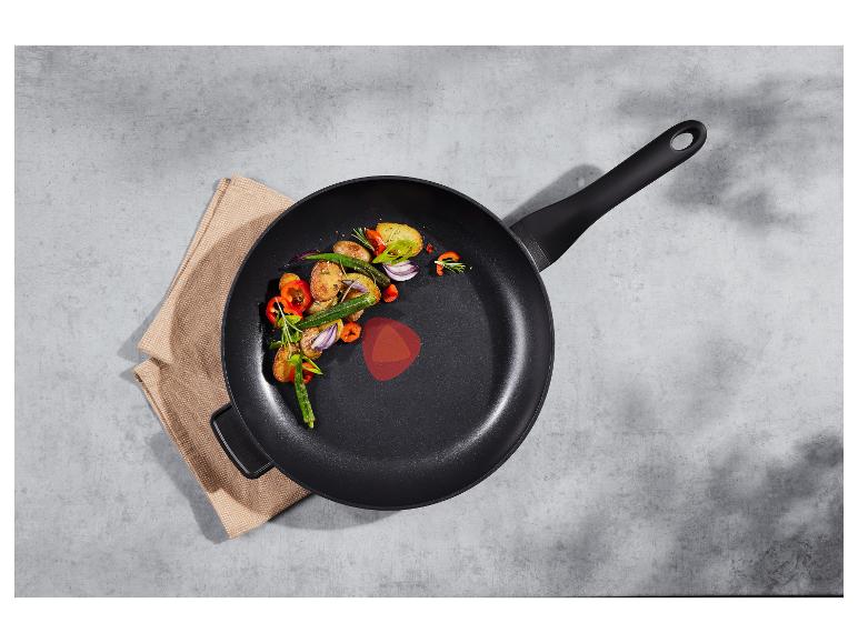 Čierna panvica s pečenou zeleninou (zemiaky, okra, paprika, cibuľa) na béžovej utierke.