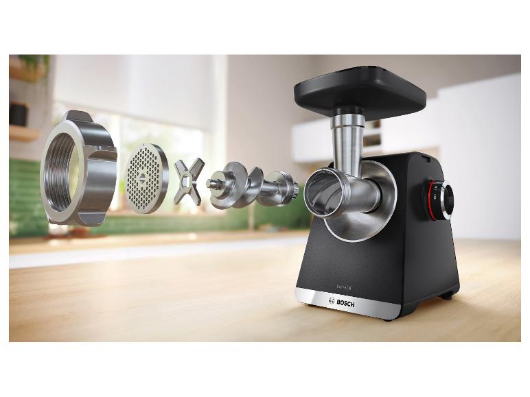 Rozložený pohľad na mlynček na mäso s jeho komponentmi rozloženými na drevenom povrchu.