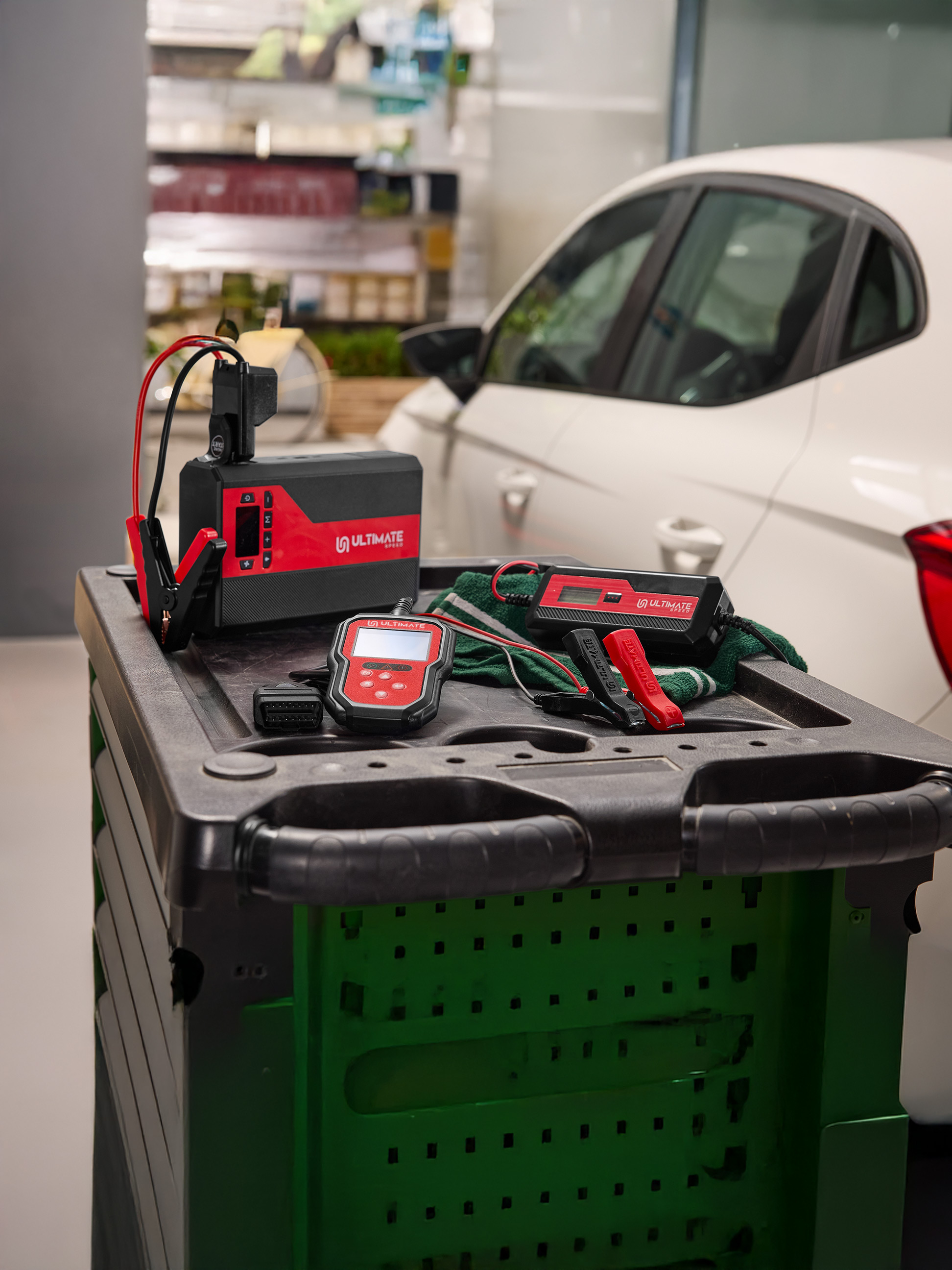 Nabíjačka autobatérií a diagnostické nástroje na vozíku vedľa bieleho auta.