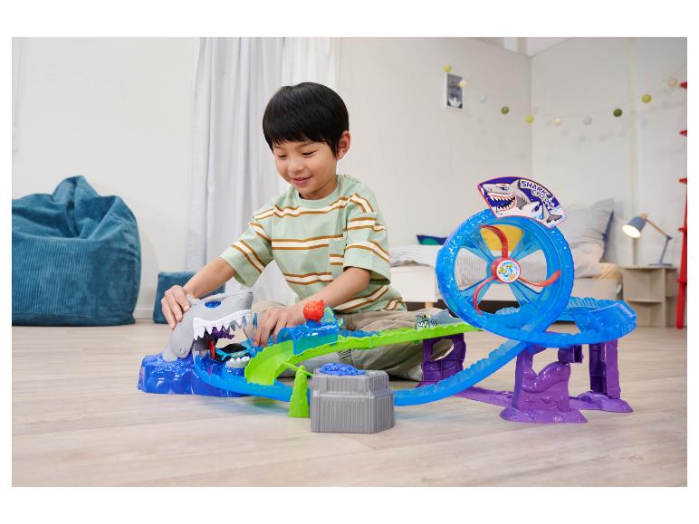 Chlapec sa hrá s hernou súpravou Hot Wheels Shark Cyclone na podlahe.