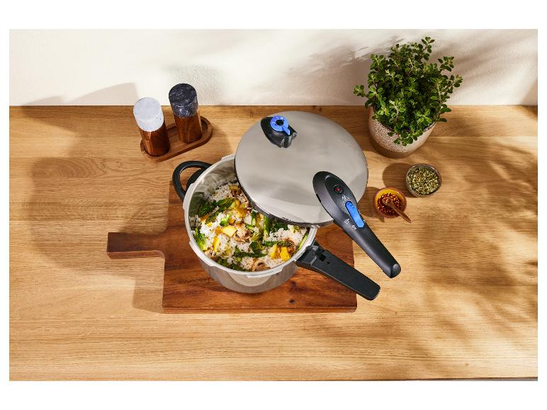 Tlakový hrniec s ryžou a zeleninou, koreninami a rastlinou na drevenom stole.