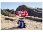 Hračka Optimus Prime stojí na skalnatom, piesočnatom teréne pod jasnou oblohou.