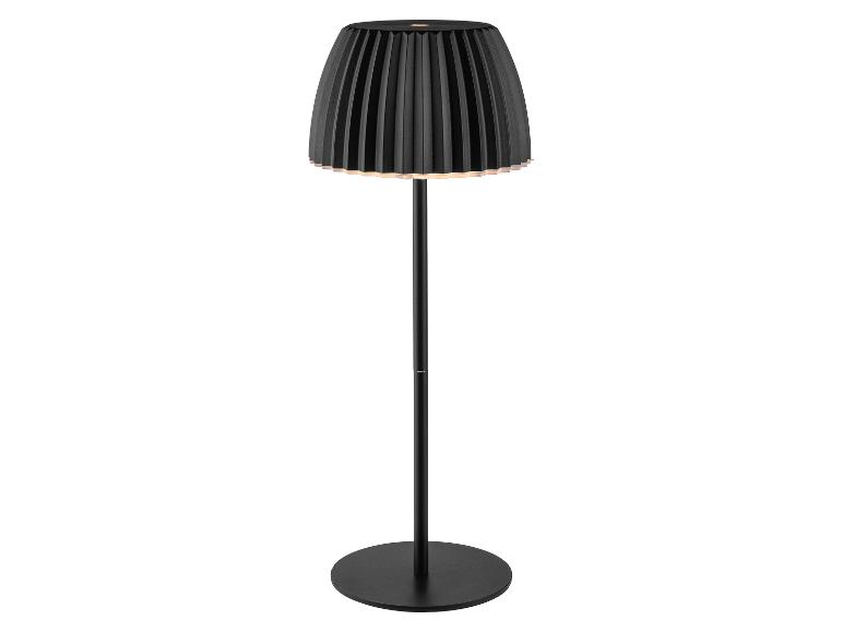 Čierna stojaca lampa s plisovaným tienidlom, vyžarujúca teplú žiaru.