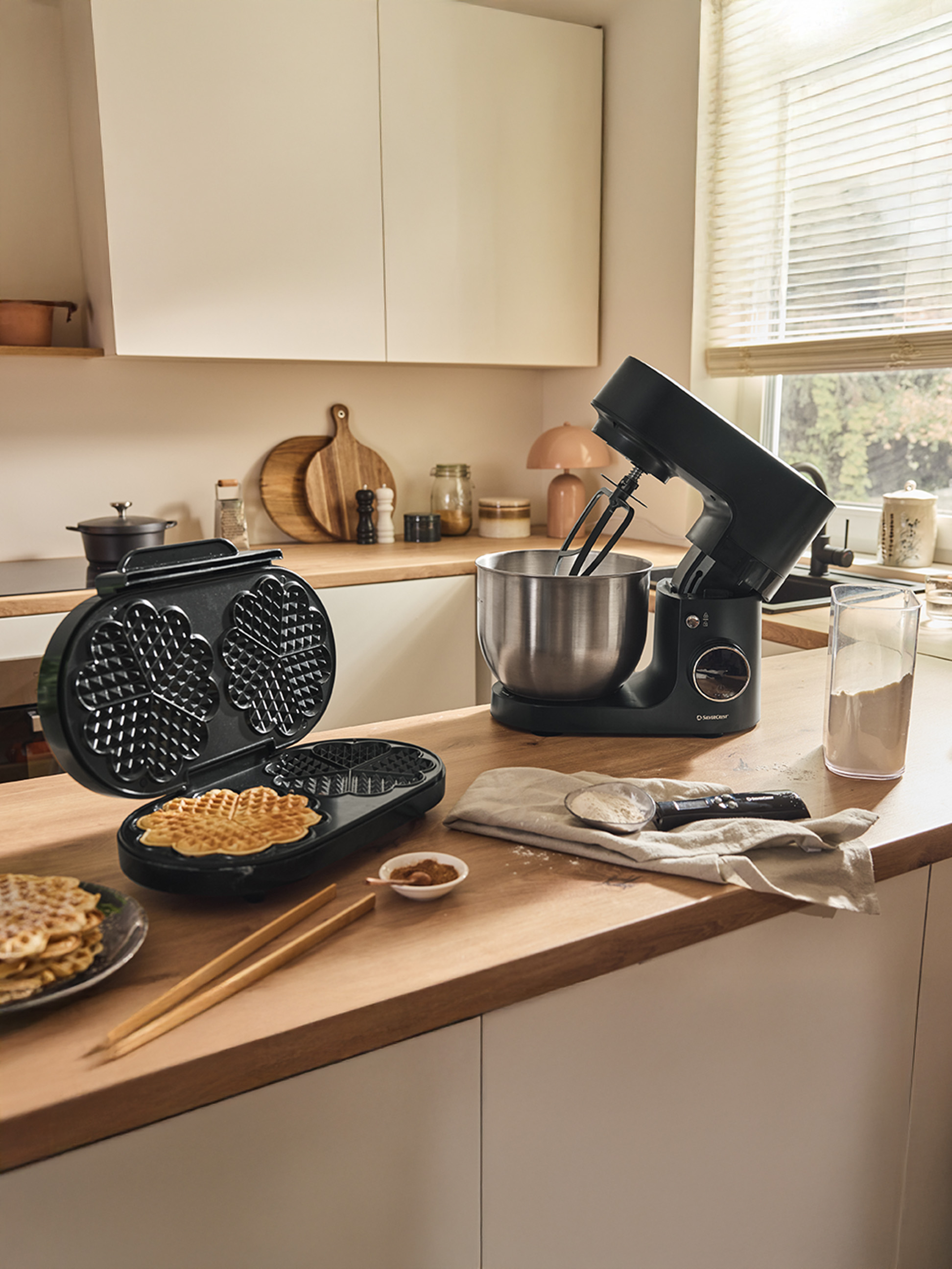 Vaflovač a čierny kuchynský mixér na drevenej doske, s hotovými vafľami.