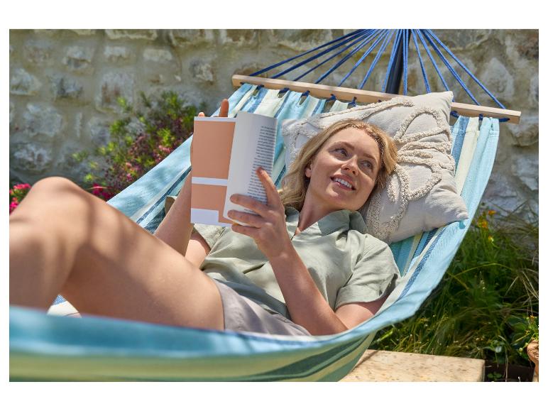 Žena relaxuje v hojdacej sieti s knihou v záhrade.
