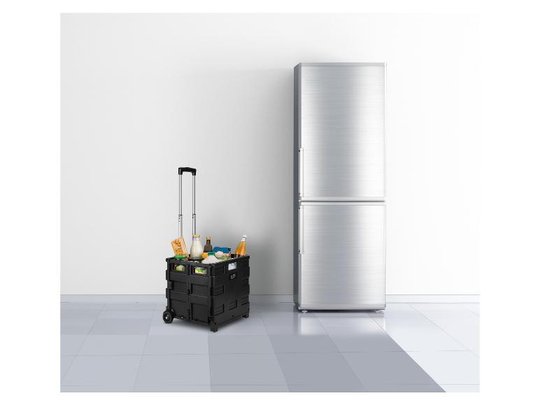 Čierny skladací nákupný vozík s potravinami vedľa striebornej chladničky.