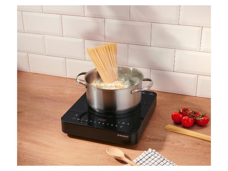 Varenie špagiet v hrnci na indukčnej varnej doske, paradajky a surové špagety na linke.