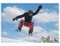 Snowboardista v čiernej bunde a červených vzorovaných nohaviciach vo vzduchu s horami
