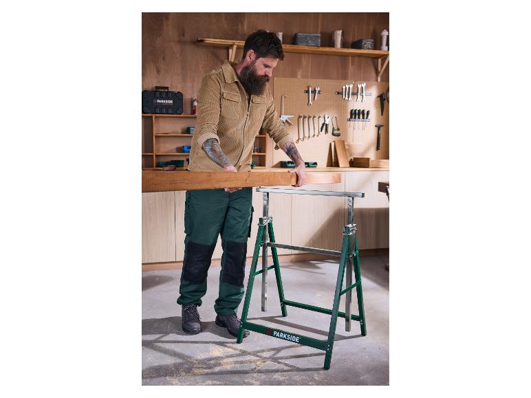 Muž kladie drevenú dosku na kozy v dielni.