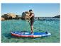 Muž na paddleboarde na čistej vode, v záchrannej veste, so skalami v pozadí.