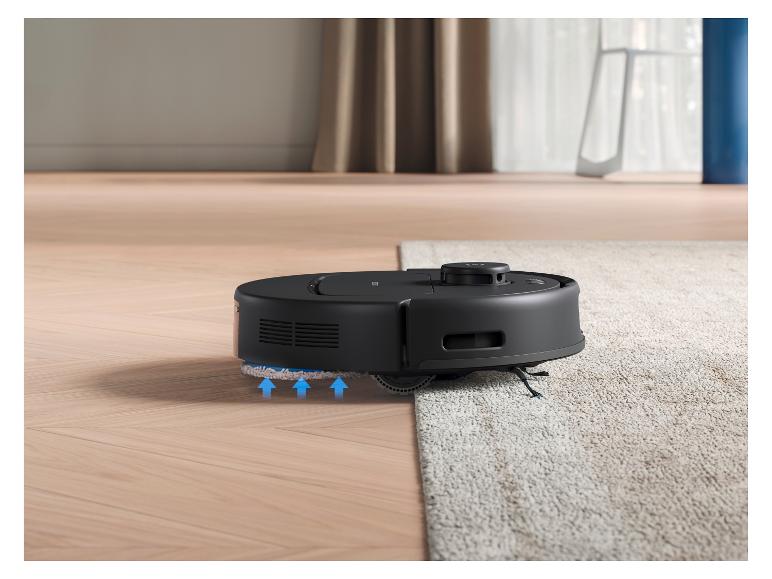 Čierny robotický vysávač prechádza z drevenej podlahy na svetlý koberec.