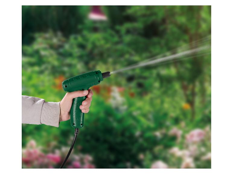 Ručná zelená striekacia pištoľ striekajúca vodu v zelenej záhrade.