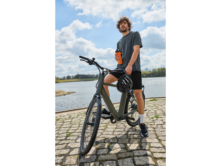 Muž na bicykli pri vode s fľašou na pitie v ruke.