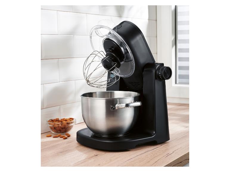 Čierny kuchynský robot s nerezovou misou a metličkou na drevenej doske.