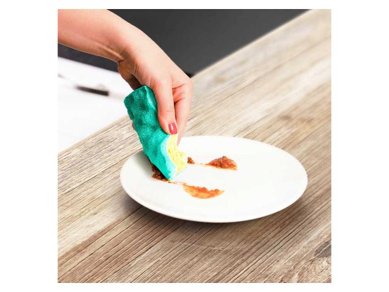 Ruka čistí tanier špongiou na riad na drevenom stole.