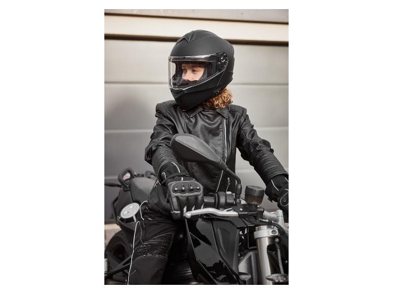 Žena v čiernej motocyklovej prilbe, koženej bunde a rukaviciach na motorke