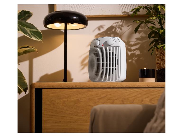 Biely ohrievač a čierna stolová lampa na drevenej skrinke.
