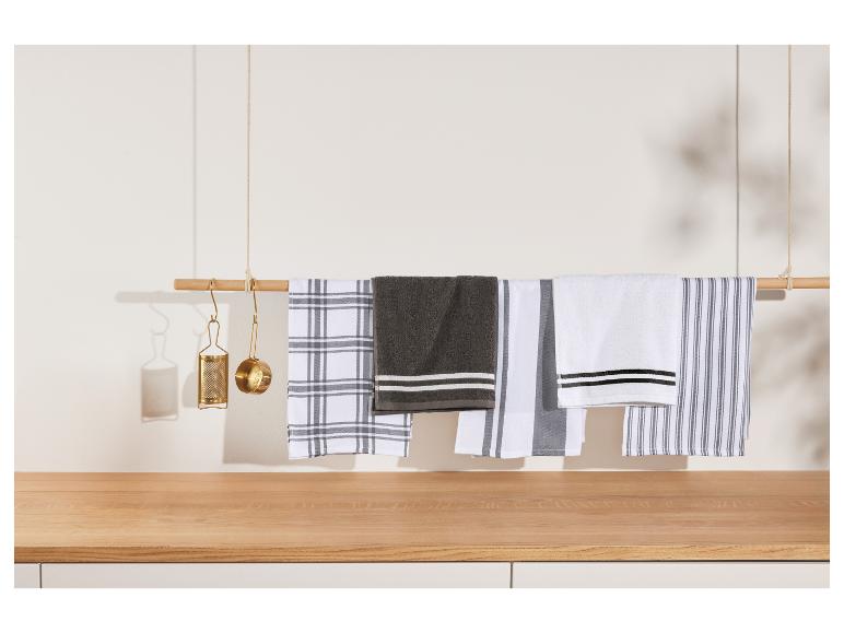 Rôzne kuchynské utierky visiace na drevenej tyči, so zlatými kuchynskými pomôckami.