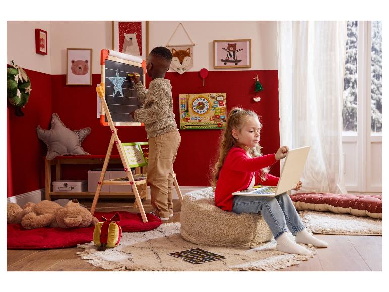 Dve deti sa hrajú vo vianočne vyzdobenej izbe: chlapec kreslí na tabuľu, dievča používa notebook.