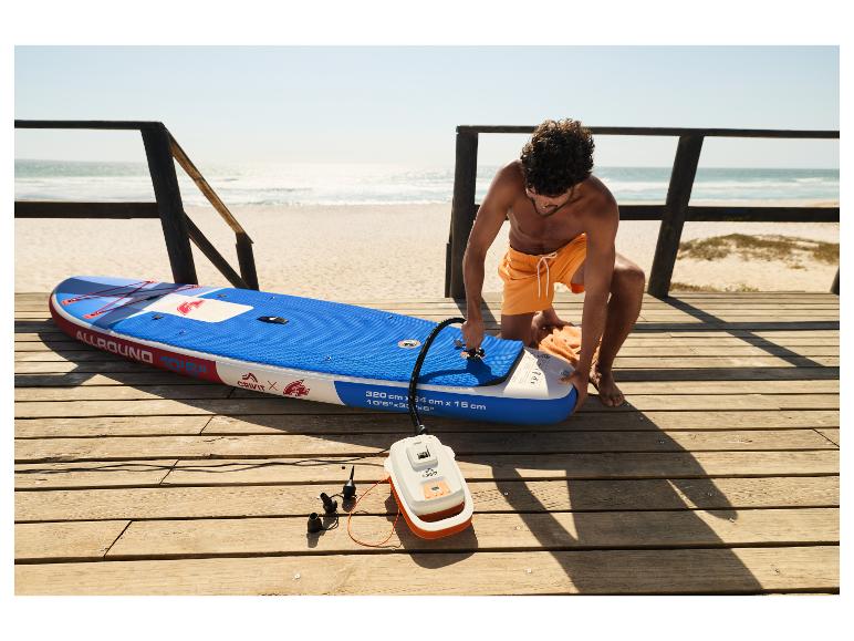 Muž nafukuje paddleboard CRIVIT na pláži elektrickou pumpou.