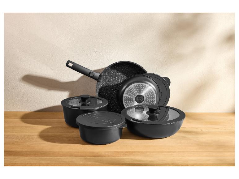 Sada čierneho kuchynského riadu, vrátane panvice, hrncov a pokrievok, na drevenej doske.