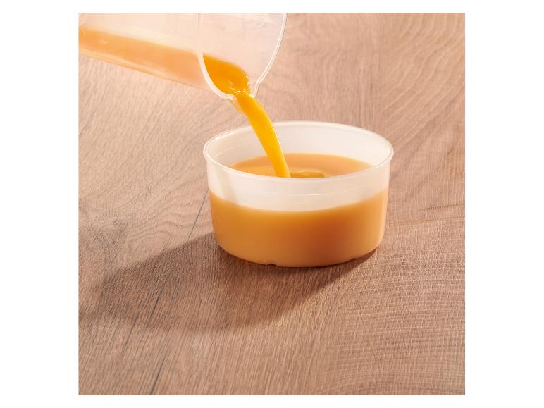 Pomarančový džús sa leje z džbánu do pohára na drevenom stole.