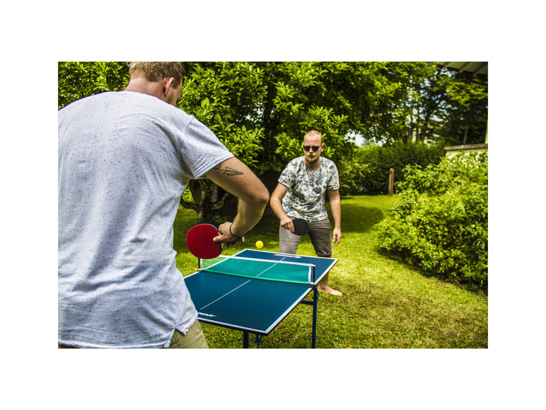 Dvaja muži hrajú stolný tenis vonku v záhrade.