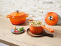Dve oranžové liatinové hrnce s pokrievkami, jeden plný polievky