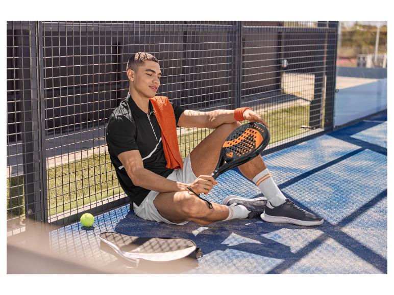Uvoľnený hráč padel tenisu so svojou raketou, sediaci pri kurte.
