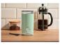 Mätovo zelený mlynček na kávu, french press kávovar a nádoba s mletou kávou na drevenom stole.
