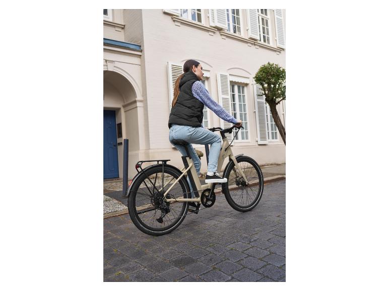 Žena jazdí na béžovom elektrickom bicykli po meste.