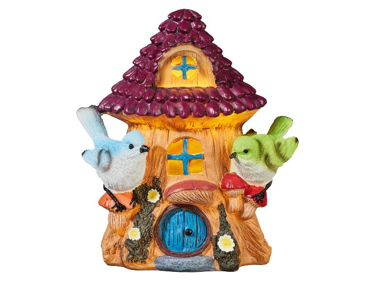 Dekoratívny rozprávkový domček s dvoma vtákmi, hubami a kvetmi, s fialovou strechou a žltými oknami.