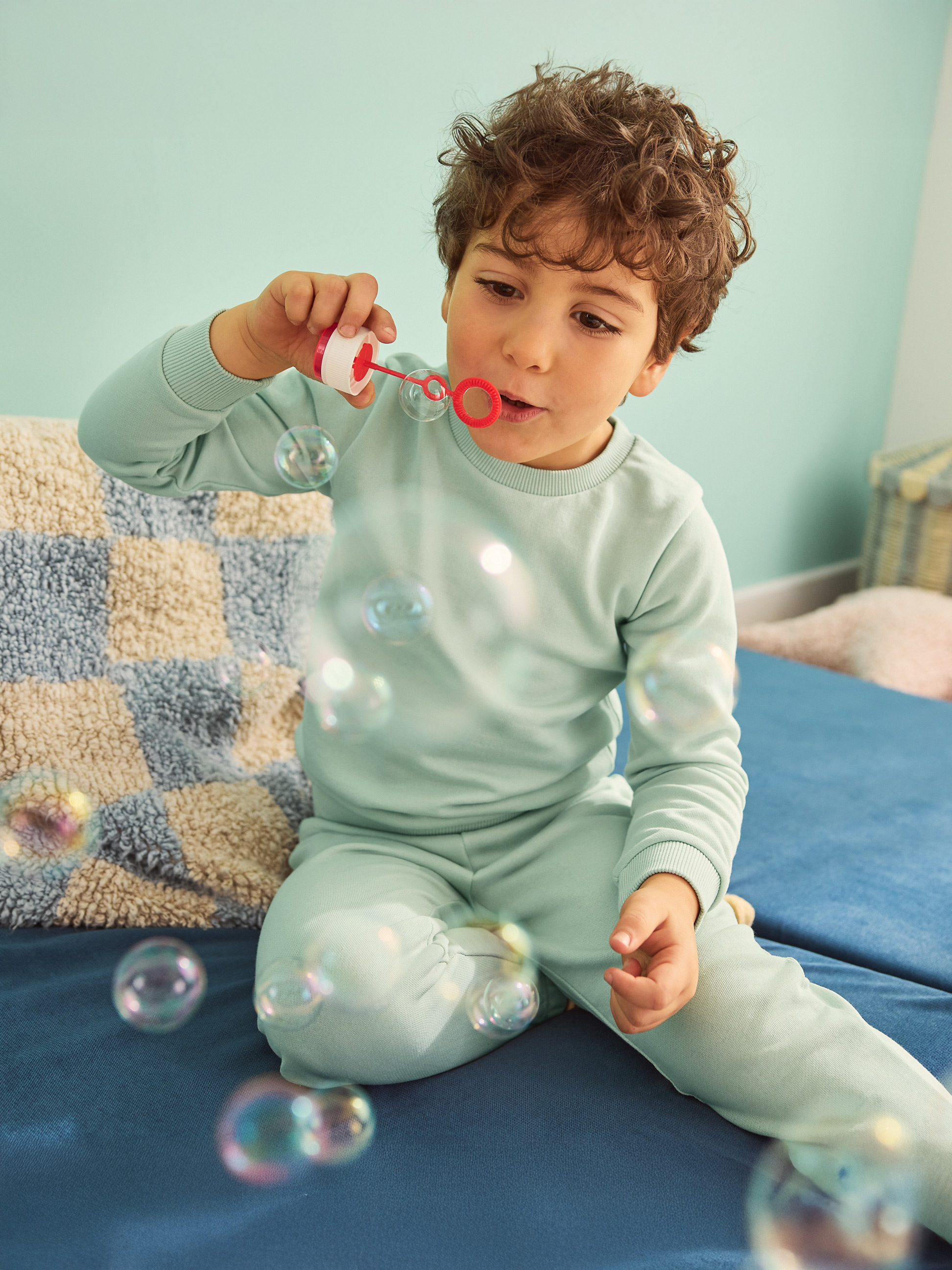 Chlapec v modrom pyžame fúka bubliny na modrej pohovke.