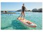 Žena v záchrannej veste na paddleboarde v čistej vode so skalami v pozadí.