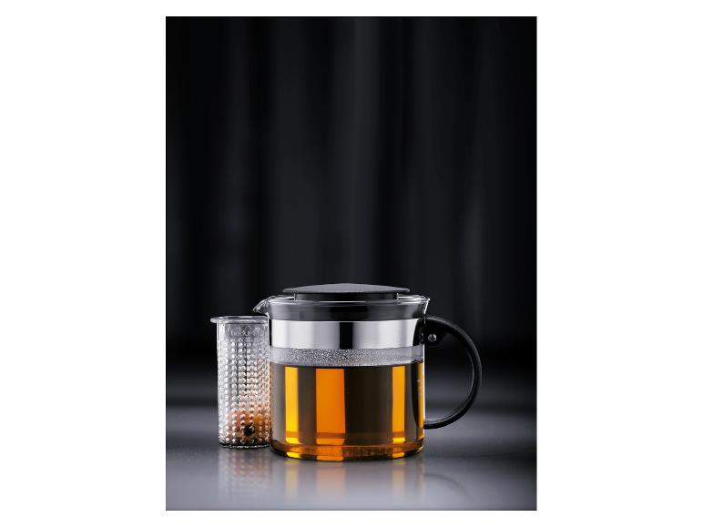 Sklenená čajová kanvica so sitkom, naplnená jantárovým čajom.