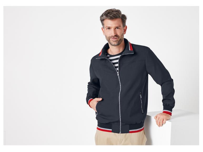 Muž má na sebe tmavomodrý bomber s červenými detailmi.