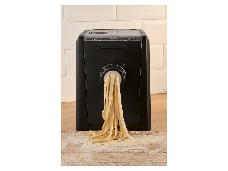 Automatický stroj na cestoviny extrudujúci čerstvé tagliatelle na pomúčenú drevenú dosku.