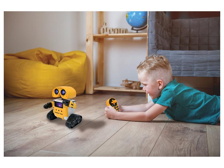 Chlapec sa hrá so žltým diaľkovo ovládaným robotom na podlahe.