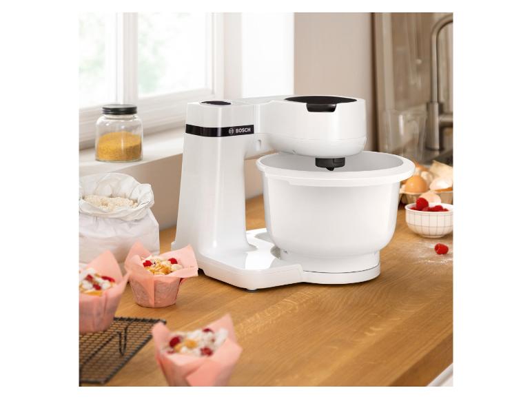 Biely kuchynský robot Bosch s muffinami a bobuľami na drevenom pulte.