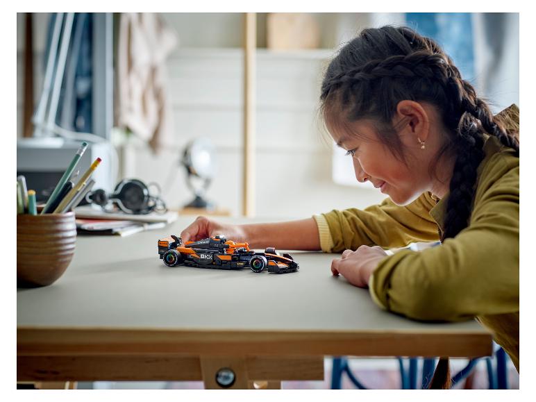 Dievča sa pozerá na čierne a oranžové pretekárske auto LEGO Speed Champions McLaren Formula 1.