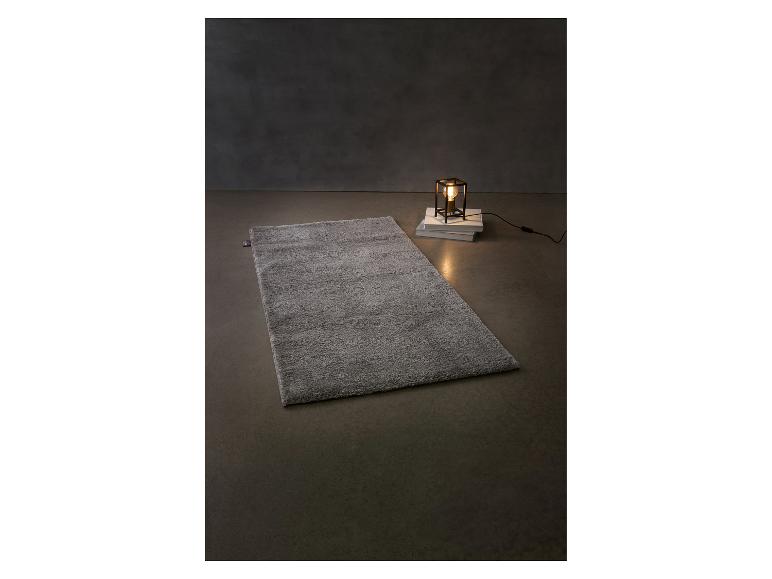Sivý huňatý koberec a stolná lampa na knihách na tmavom pozadí.