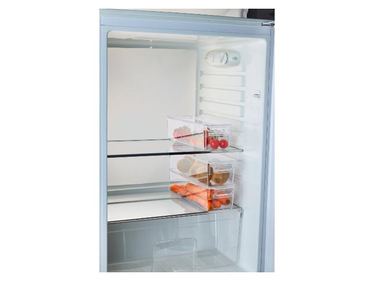 Chladnička s priehľadnými nádobami plnými paradajok, kiwi a mrkvy.