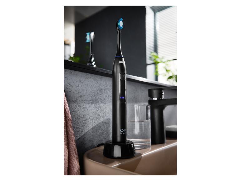 Čierna elektrická zubná kefka v nabíjačke vedľa kúpeľňového umývadla.