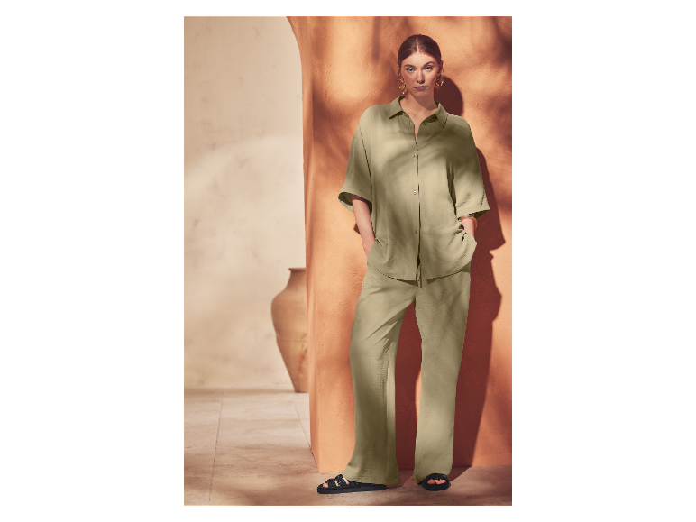 Žena pózuje v svetlozelenom kostýme a čiernych sandáloch.