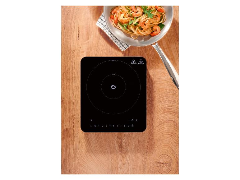 Indukčná varná doska s panvicou krevetových cestovín na drevenom povrchu.