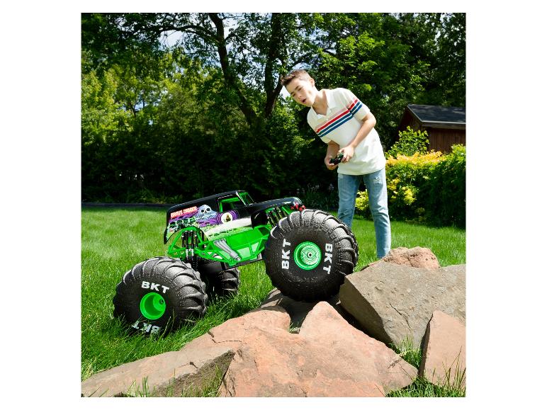 Chlapec ovláda RC monster truck Grave Digger na tráve, s kameňmi v popredí.